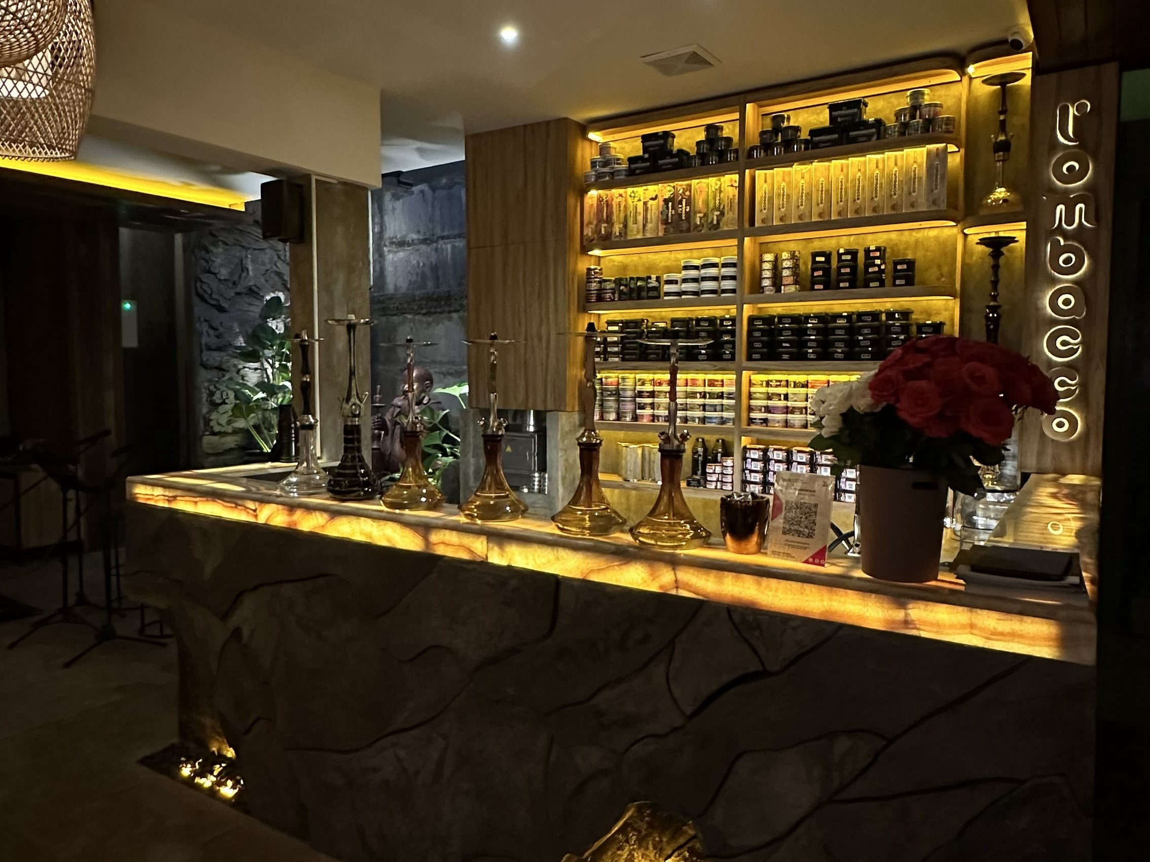 A stylish hookah lounge bar showing off various premium setups and tobacco flavors on the shelves. Visiting a professional spot like this is a great way to test out different styles before buying the best hookah pipe for your own home.