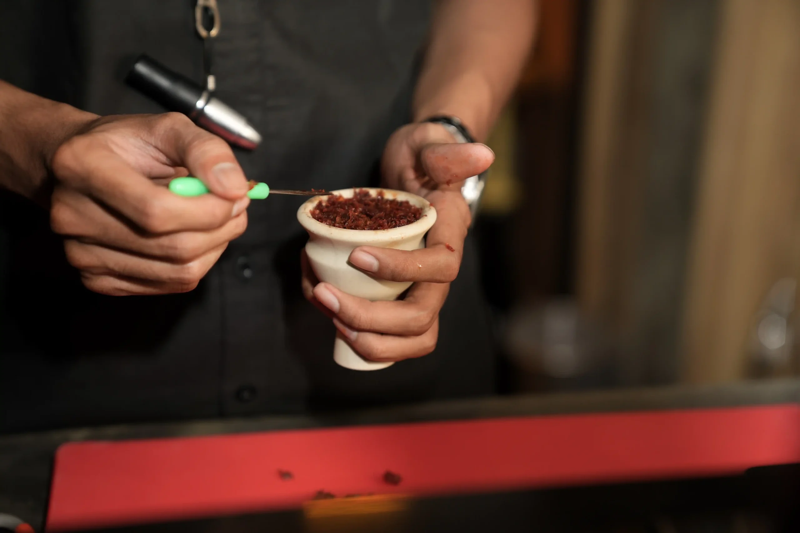 A close-up view of someone's hands carefully packing premium red tobacco into a white bowl to ensure a smooth and long-lasting hookah bali smoke.