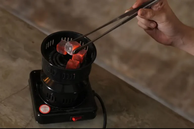 A close-up of someone carefully using tongs to place glowing coconut coals on an electric stove, getting ready for a perfect hookah bali session.