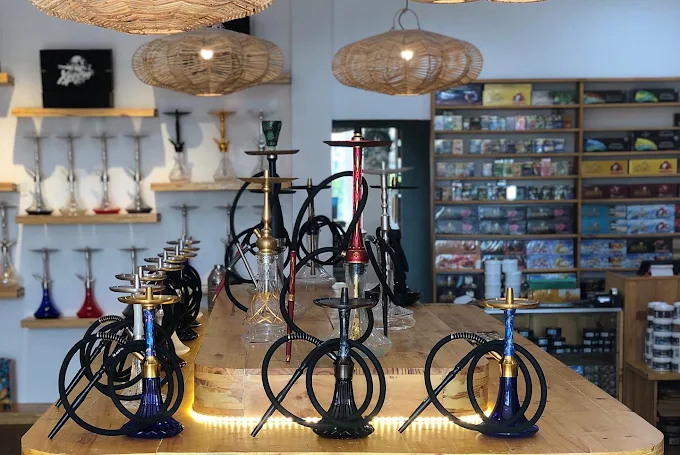 A central display table featuring fully assembled modern hookahs and accessories under rattan lights. If you're wondering what to look for when you buy shisha in Bali, checking out complete setups like these in a well-stocked retail store is the perfect place to start.