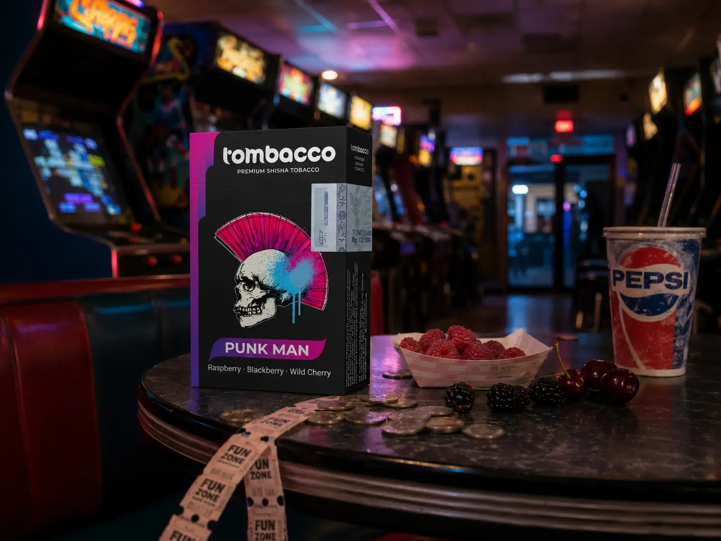 A box of Tombacco Punk Man shisha tobacco featuring an edgy skull with a pink mohawk, set on a retro arcade table. Surrounded by fresh raspberries, blackberries, wild cherries, and arcade tickets, it highlights fun and vivid Adalya flavor alternatives.