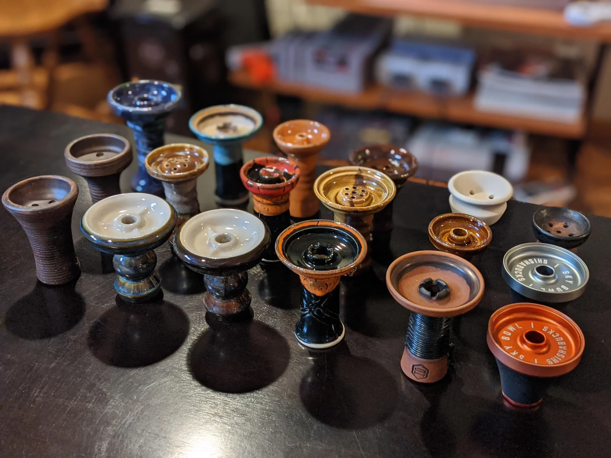 A wide variety of hookah bowl types displayed together on a table, showcasing the different shapes, sizes, and materials available for building the ultimate shisha setup.